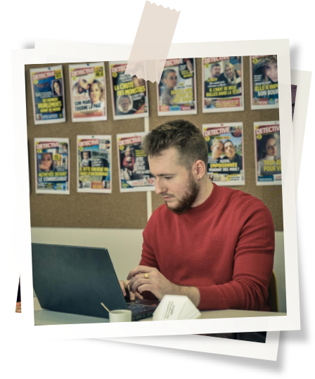 L'image représente l'auteur du livre "Tremblez", concentré et absorbé par son travail d'écriture. Assis à un bureau, il tape sur un ordinateur portable tout en regardant attentivement l'écran, habillé d'un pull rouge qui contraste avec l'environnement. Derrière lui, un tableau d'affichage orné de nombreuses couvertures de magazines de style "True Crime" évoquant des histoires de détectives et de faits divers, renforçant l'ambiance de mystère et de suspense qui semble entourer son univers littéraire. Le cadrage de l'image, encadrée dans un style de photo Polaroid avec du ruban adhésif au-dessus, ajoute une touche personnelle et authentique à la présentation de l'auteur, comme s'il s'agissait d'un moment pris sur le vif dans son quotidien créatif.